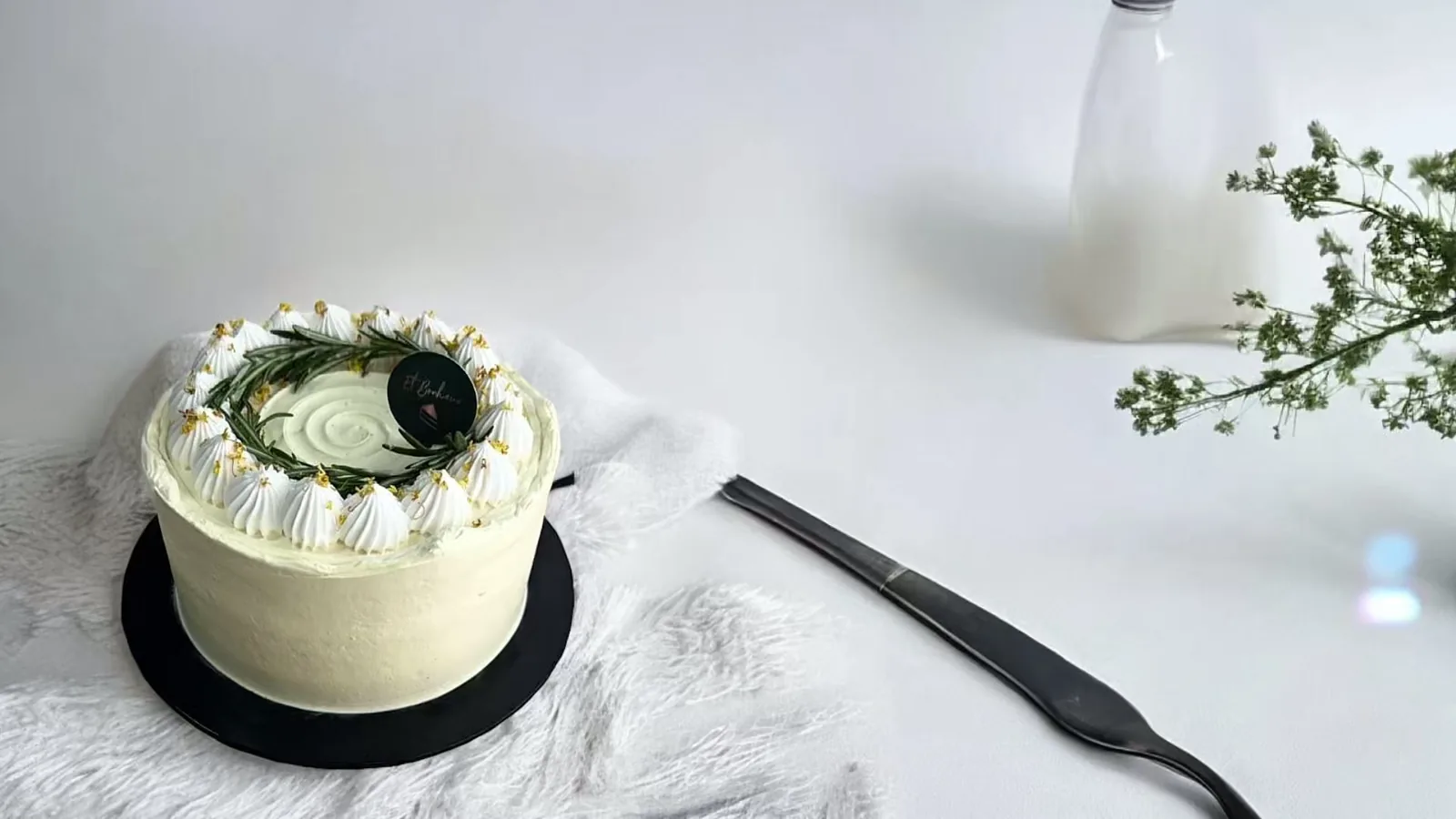 Round cake with white frosting, piped borders, chamomile flowers and chocolate disc centerpiece