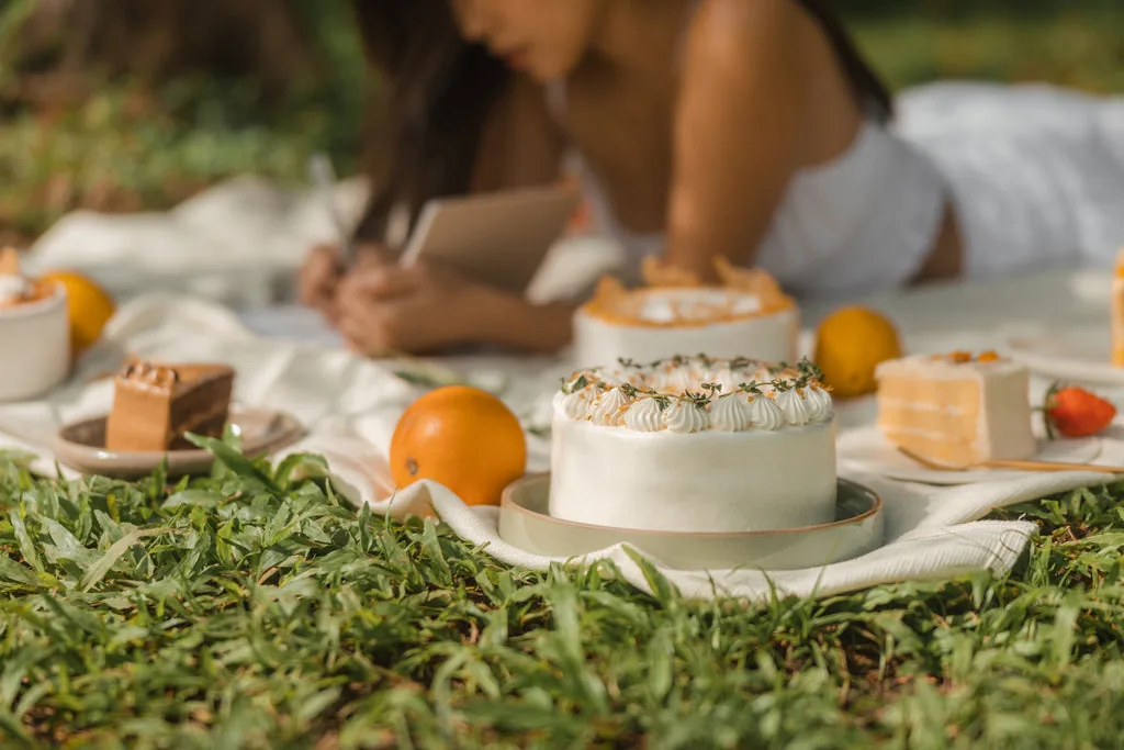 Decorated cakes and pastries arranged on grass for an outdoor picnic display