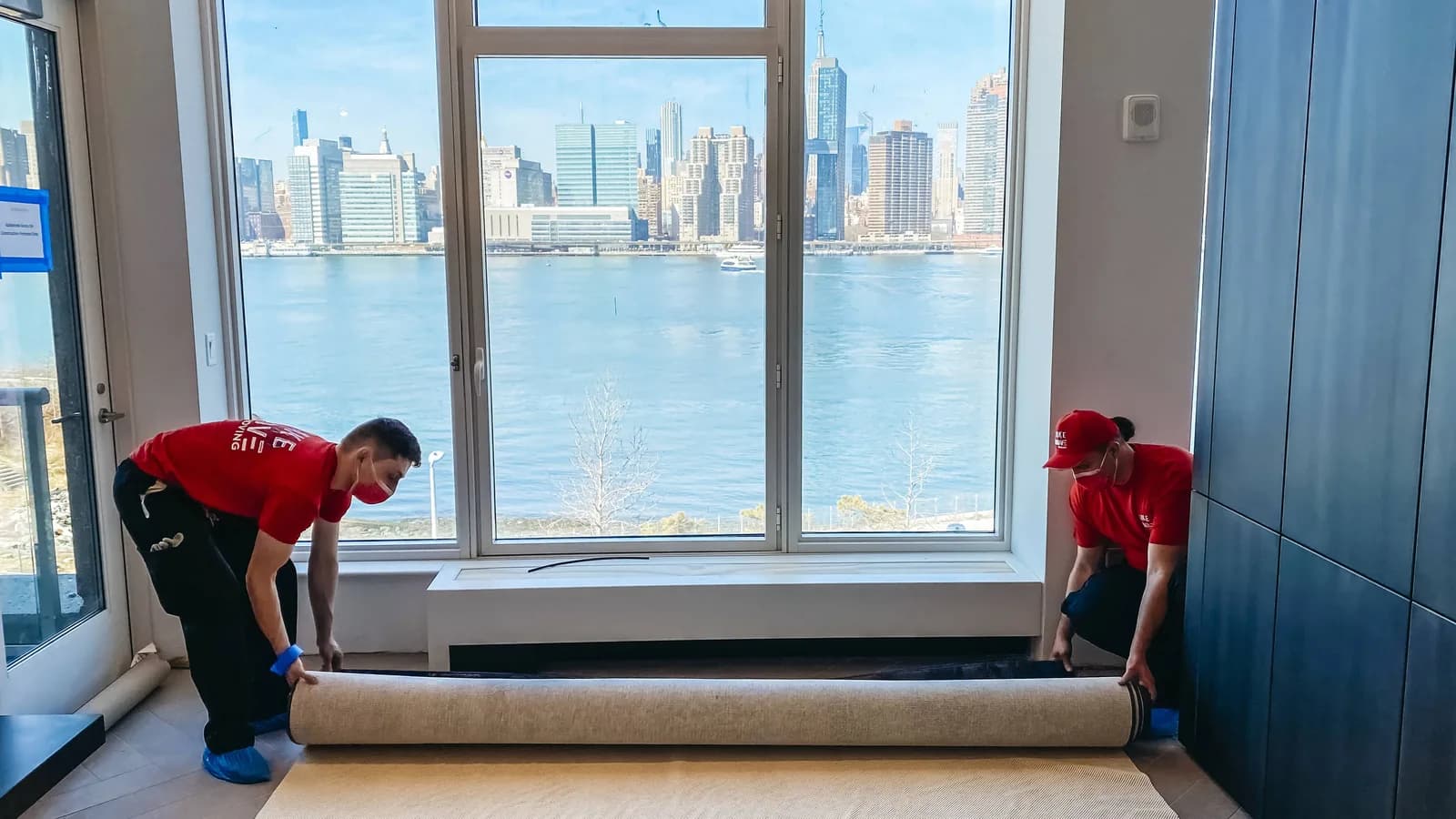 Movers unrolling flooring in apartment overlooking cityscape and water