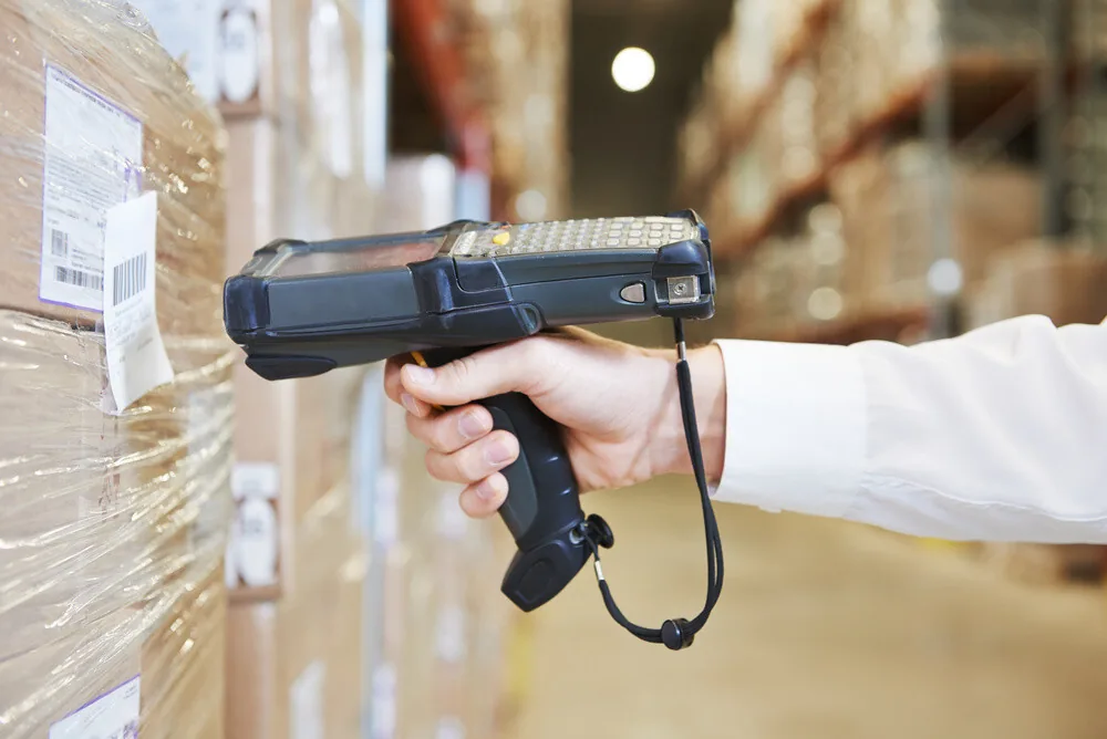 Worker scanning barcode on wrapped package in warehouse with boxes in background