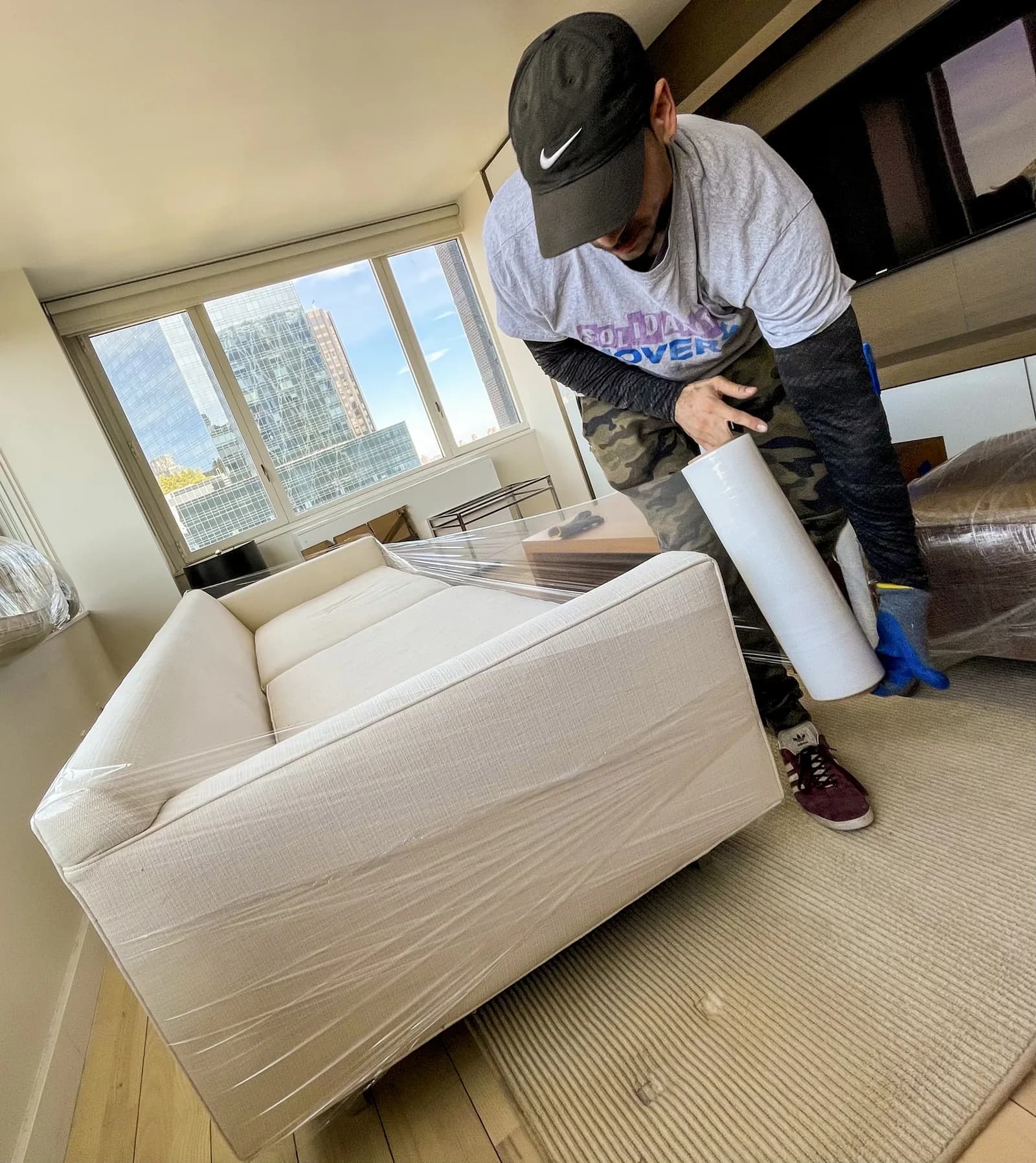 Worker wrapping furniture with plastic at a moving job in a high-rise apartment