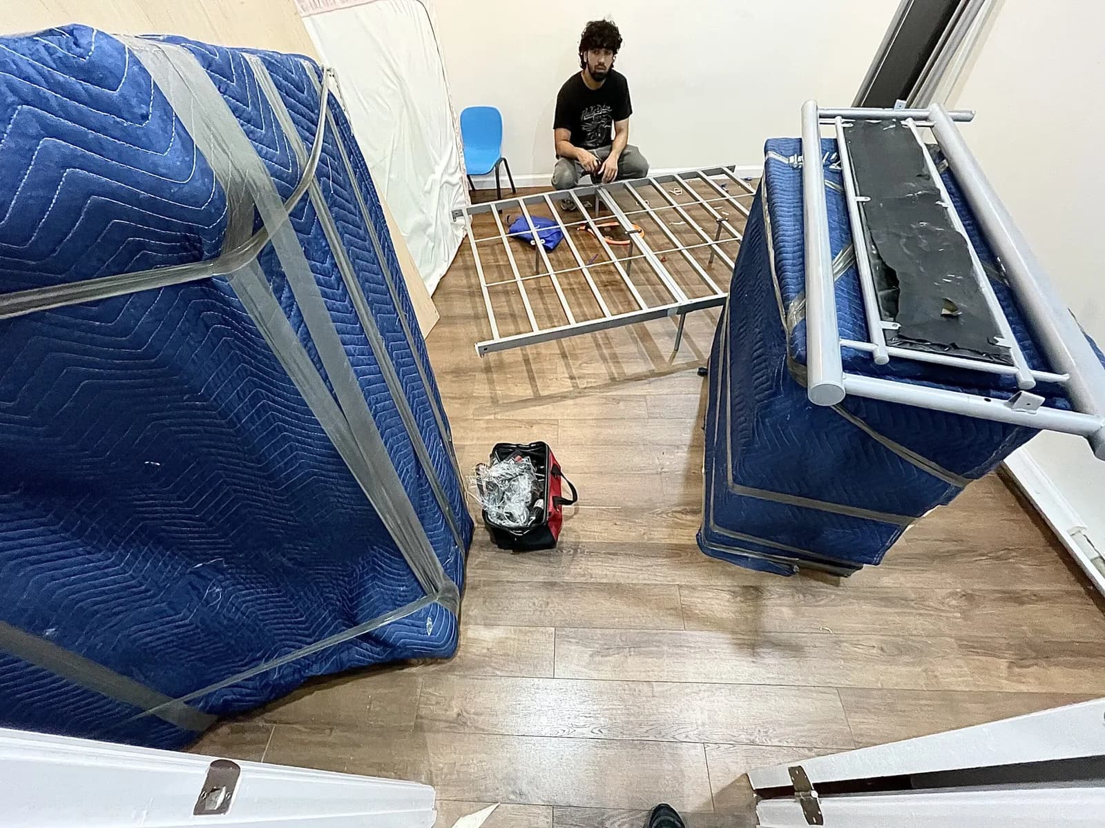 Mover wrapping furniture with blue quilted blankets in preparation for transport
