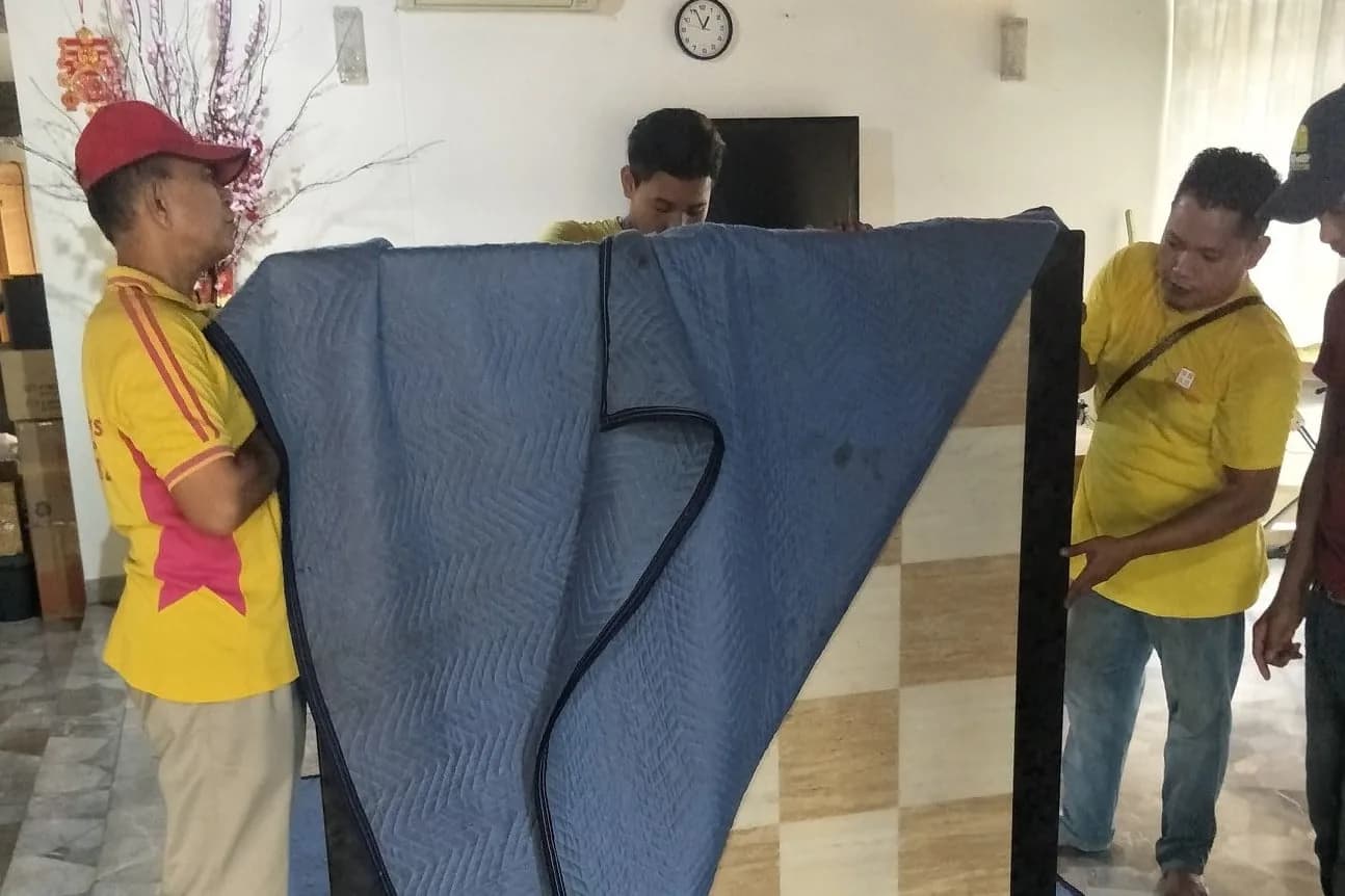 Moving company workers wrapping and handling a mattress with protective blue padding
