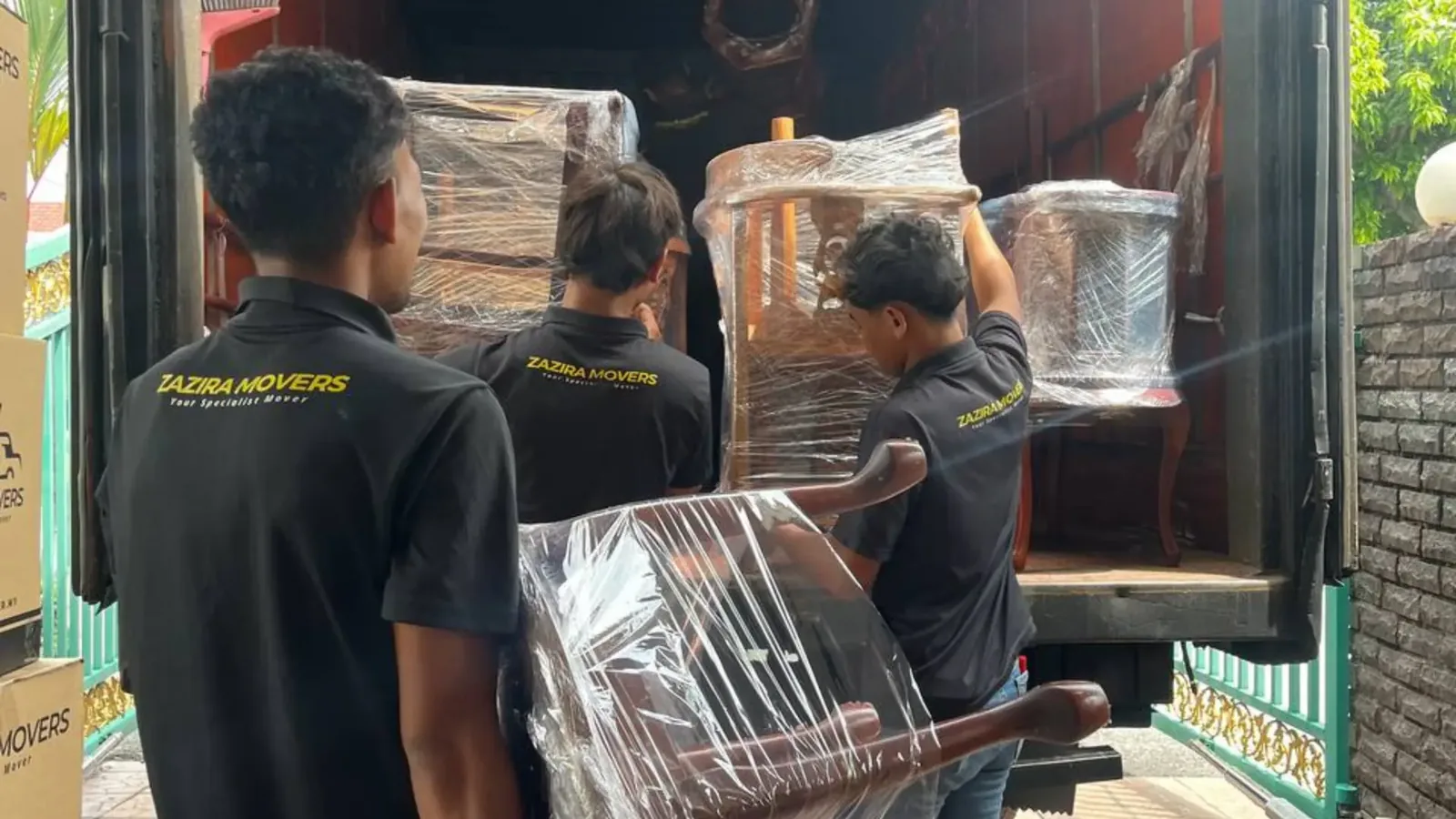 Moving crew in Zazira Movers uniforms loading wrapped furniture into a truck