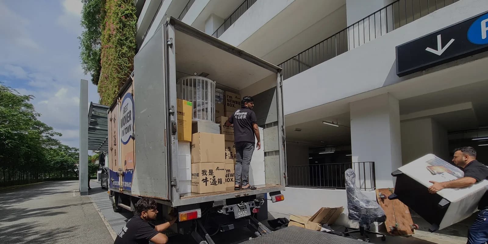 Moving company workers loading cardboard boxes and furniture into a transport truck at building entrance.