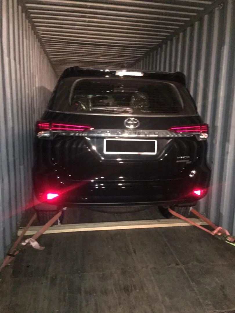 Black Toyota vehicle on transport dolly inside a metal shipping container