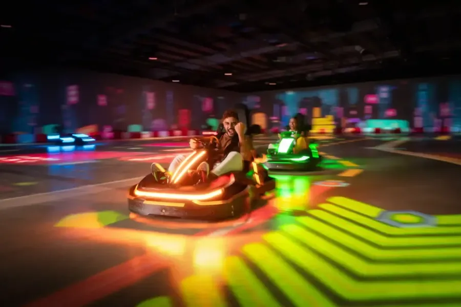 Neon-lit electric go-karts racing on an indoor track with glowing floor patterns and colorful lighting