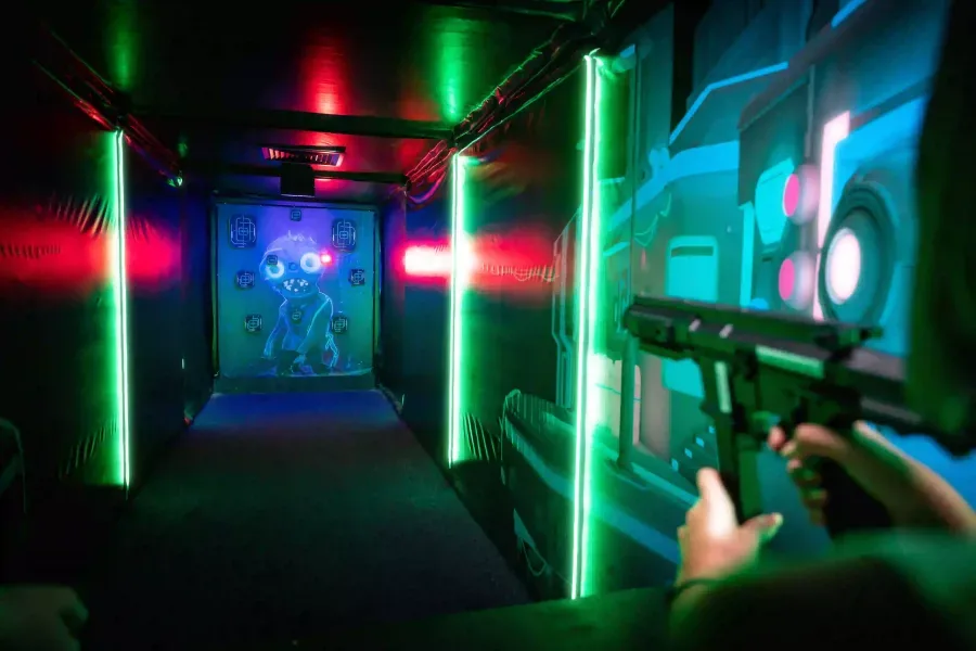 Neon-lit laser tag arena with glowing green pillars, game screens, and player with laser gun