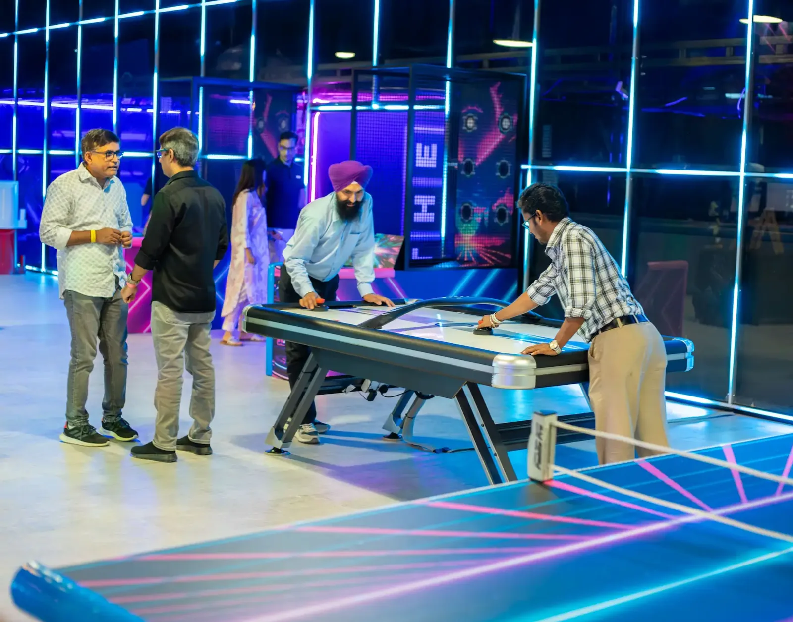 Players enjoy air hockey in a neon-lit entertainment center with colorful gaming decor