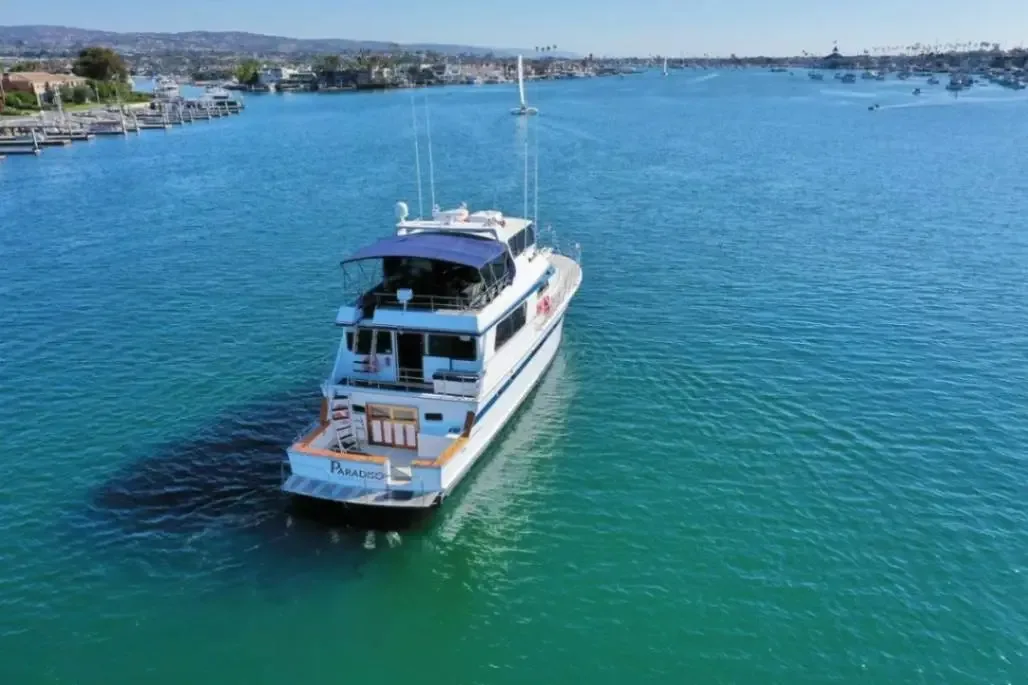 White motor yacht with blue accents anchored in turquoise water near residential waterfront