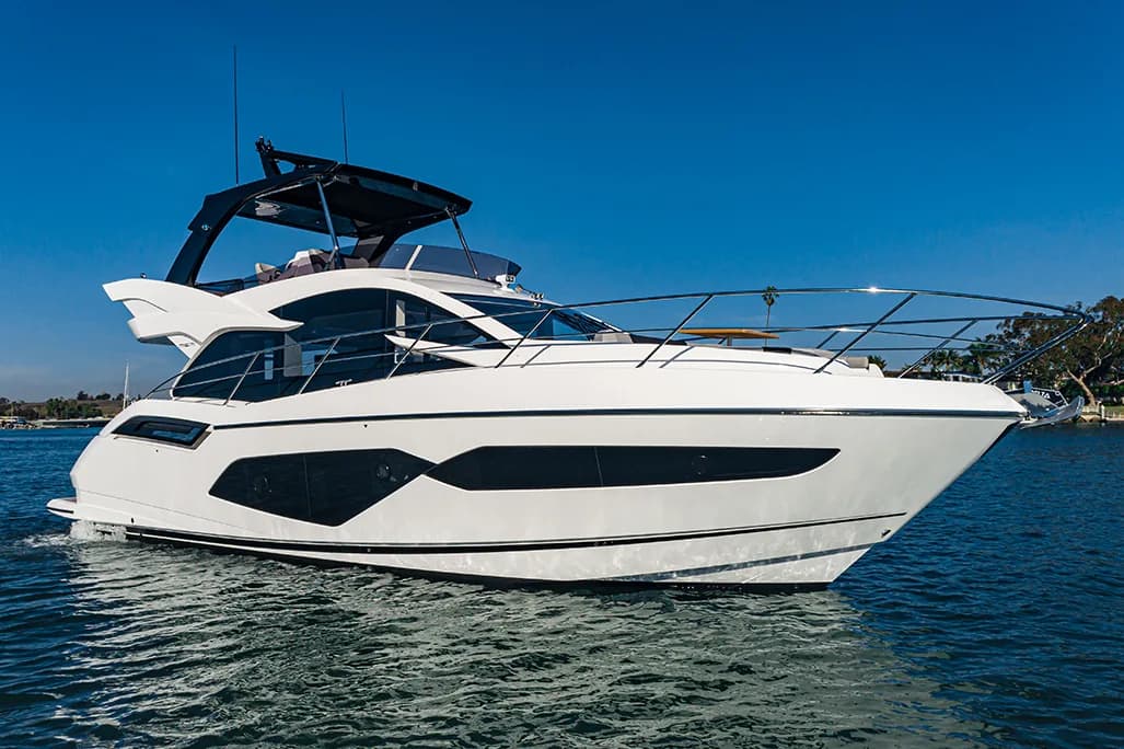 Modern white and blue multi-deck yacht anchored in clear blue water with palm trees visible on the shoreline