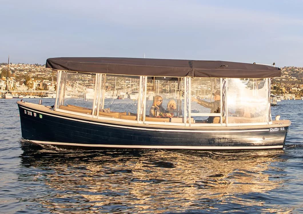 Enclosed tour boat with passengers in a scenic coastal harbor surrounded by hills