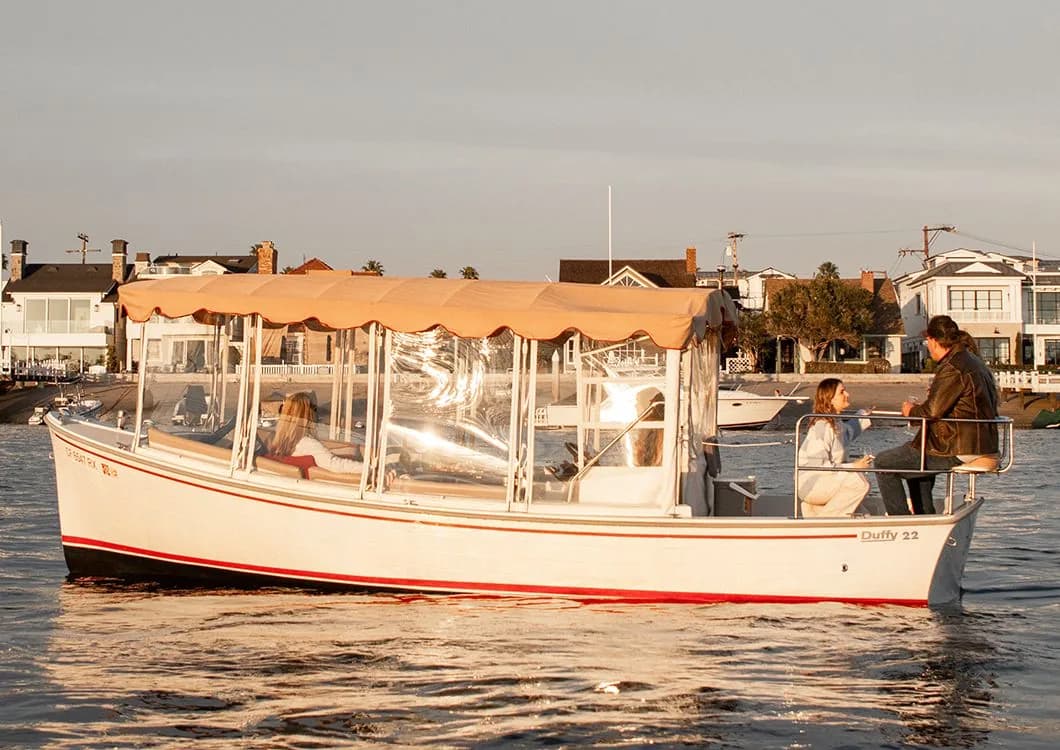White passenger boat with orange canopy carrying tourists on Newport Harbor with waterfront homes behind