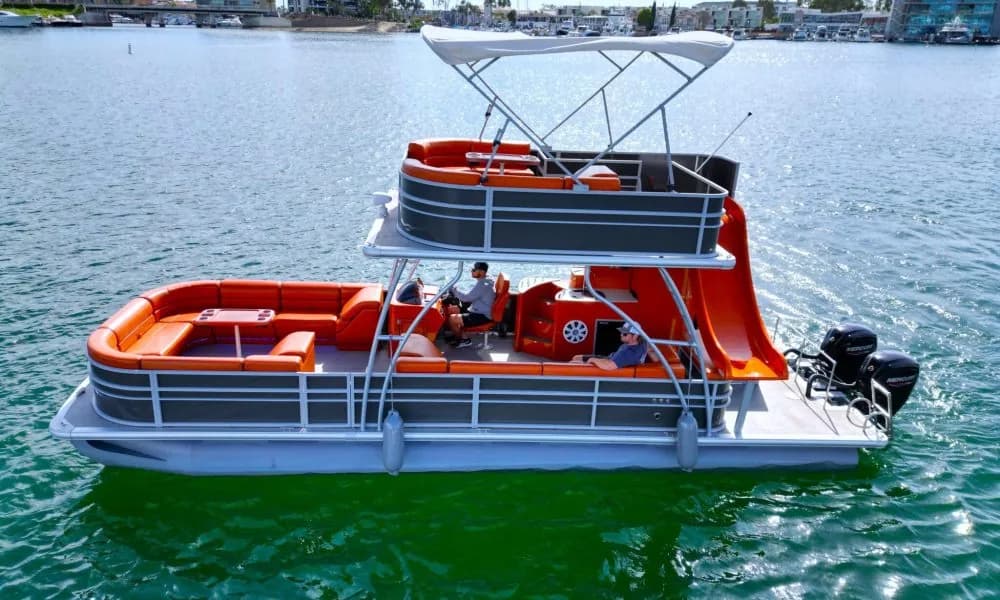 Two-deck pontoon party boat with orange seating and canopy on water