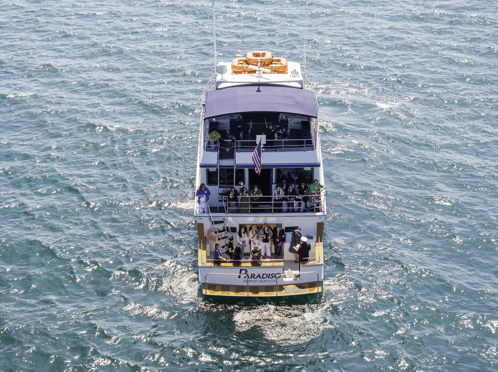 Multi-deck white party yacht Paradise with passengers on decks in open ocean water
