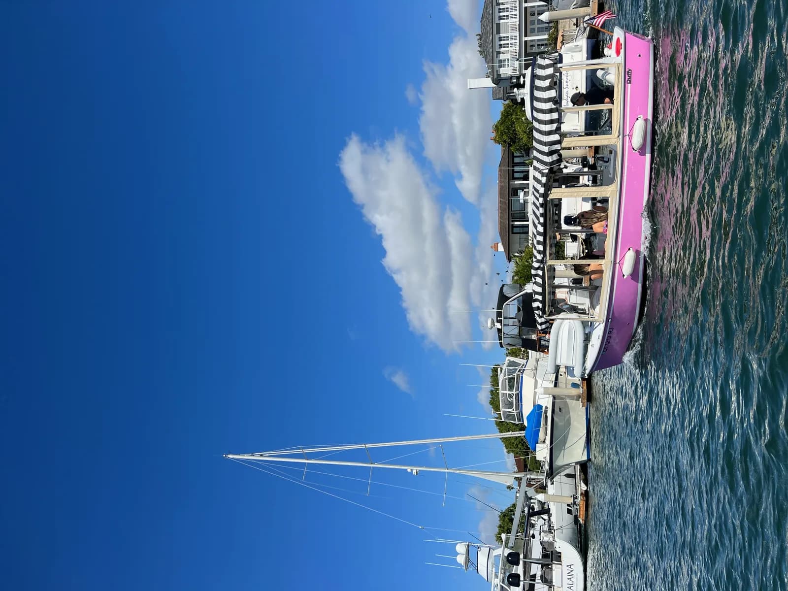 Pink and white party boat with striped awning docked at waterfront pier