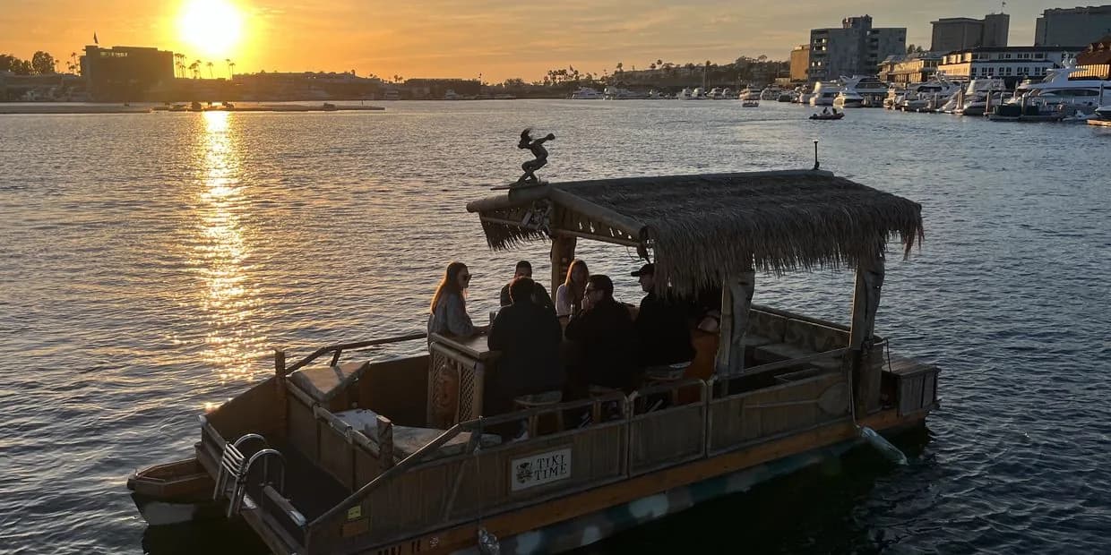 Tiki party boat with passengers and palm-thatched canopy on water at sunset