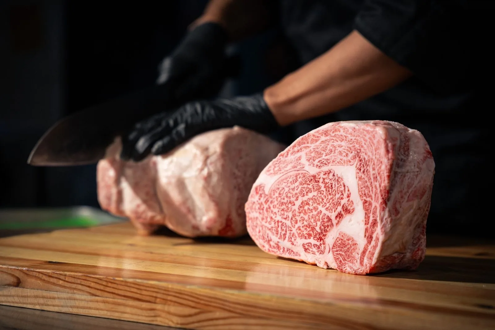 Premium marbled wagyu beef steaks on wooden board with chef in background
