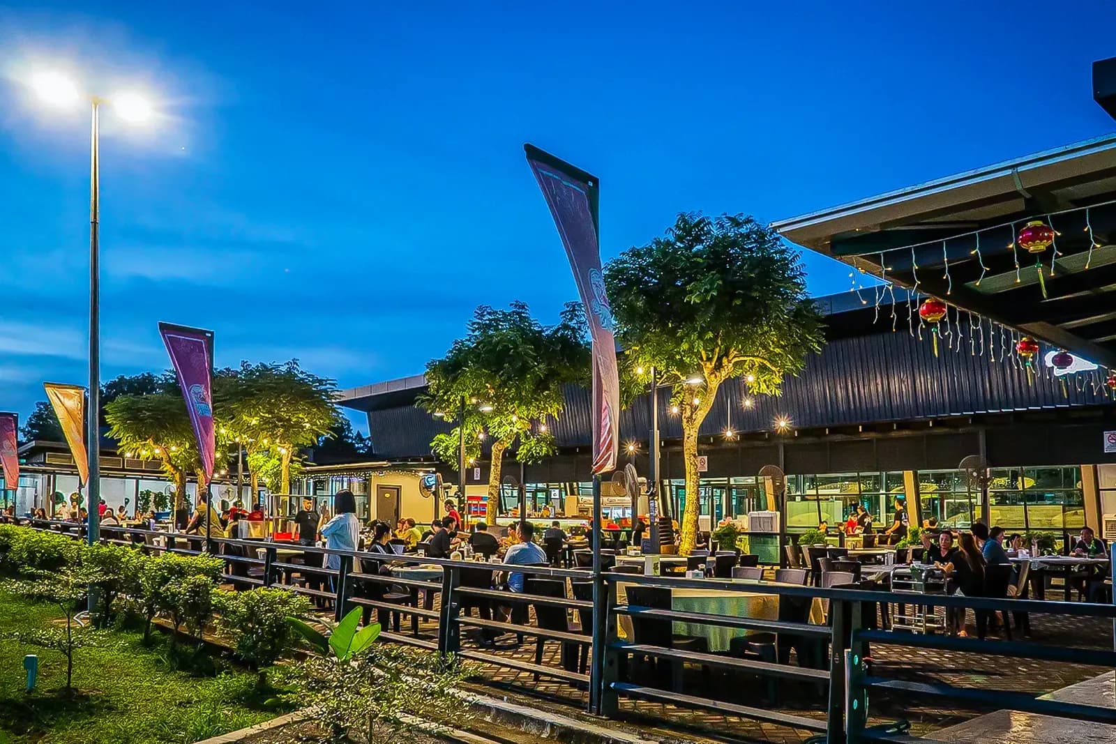 Outdoor seafood restaurant at dusk with lit trees, wooden tables, and customers dining under covered structures