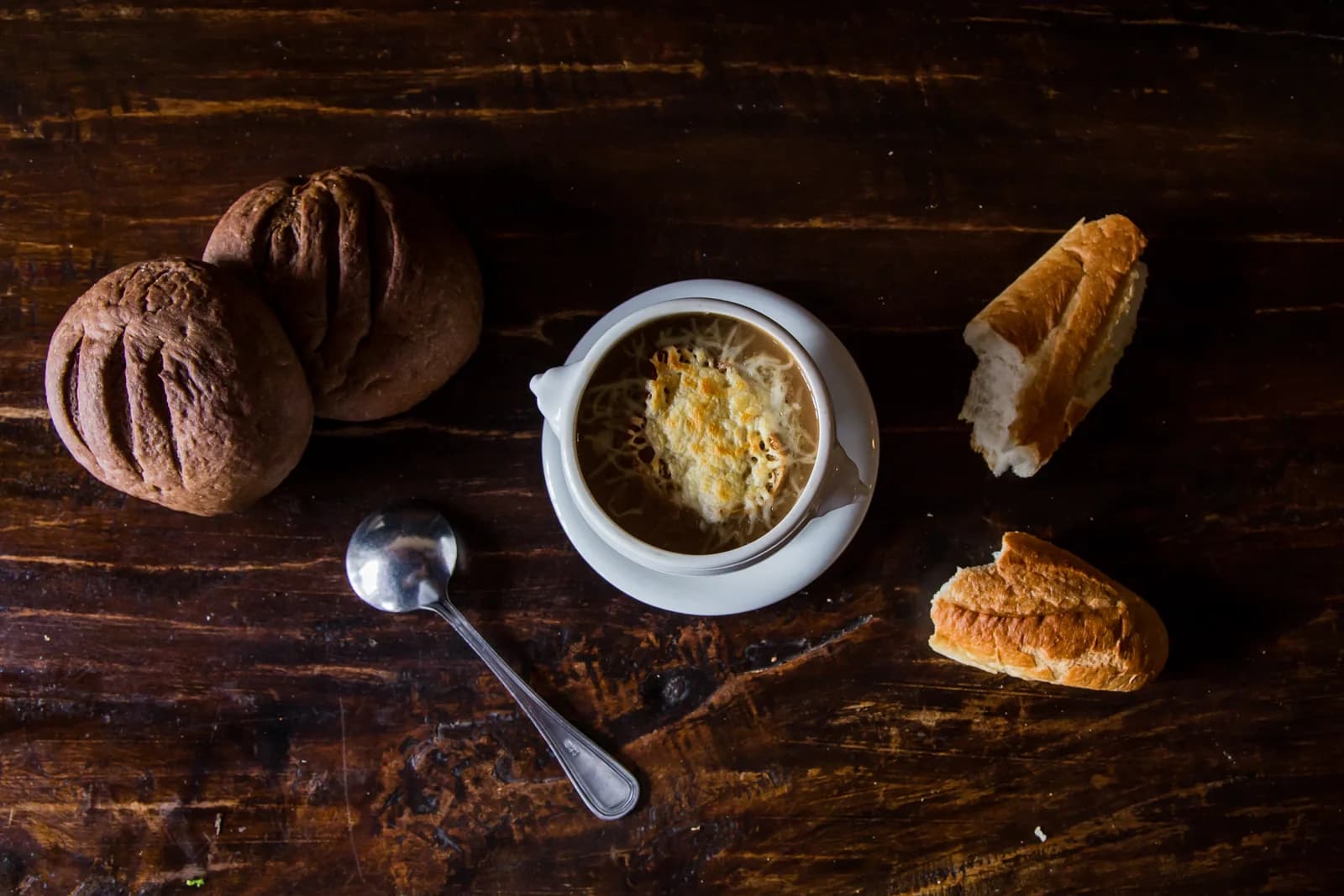 Assorted French breads and a bowl of soup arranged on weathered wood table