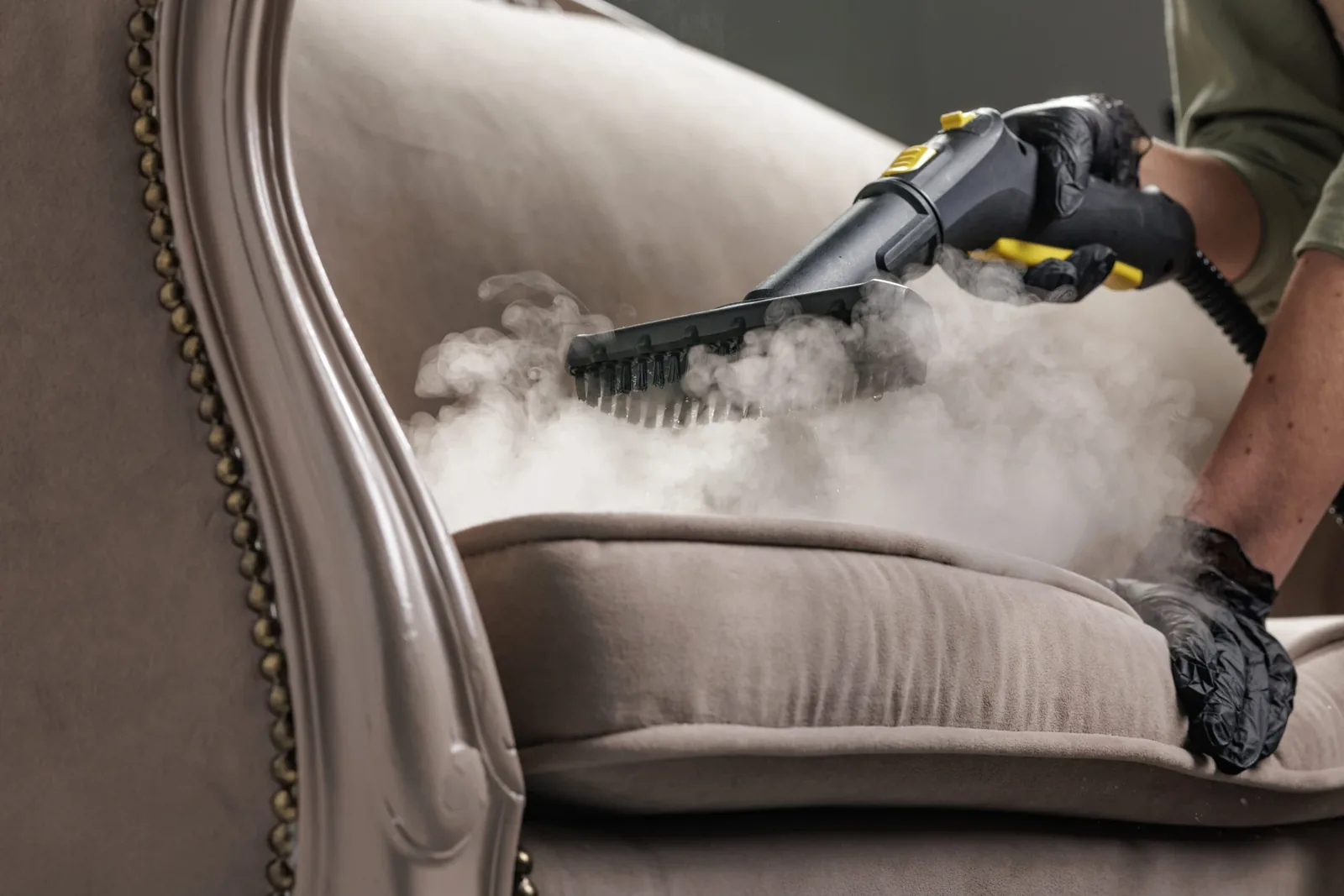 Worker steam cleaning an upholstered chair cushion with professional equipment