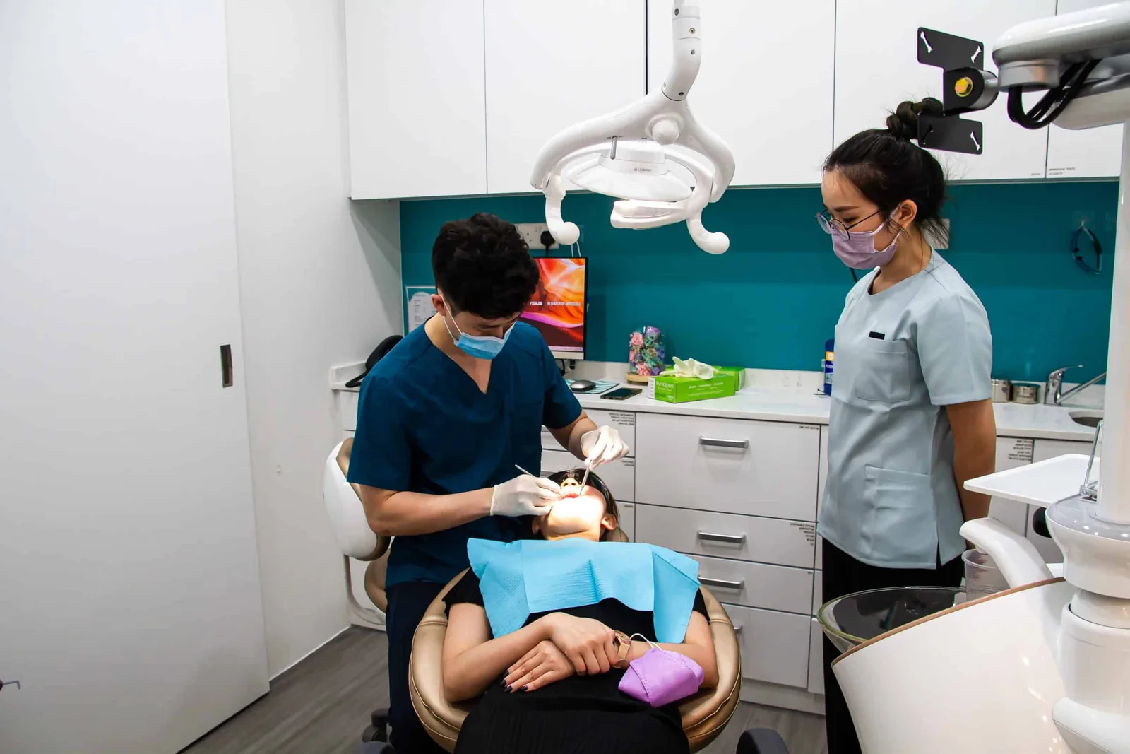 Dentist treating patient in clinical setting with assistant nearby