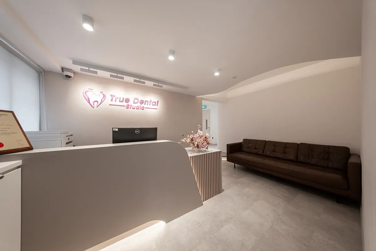 Modern dental clinic reception area with white desk, neon signage, and brown waiting seating