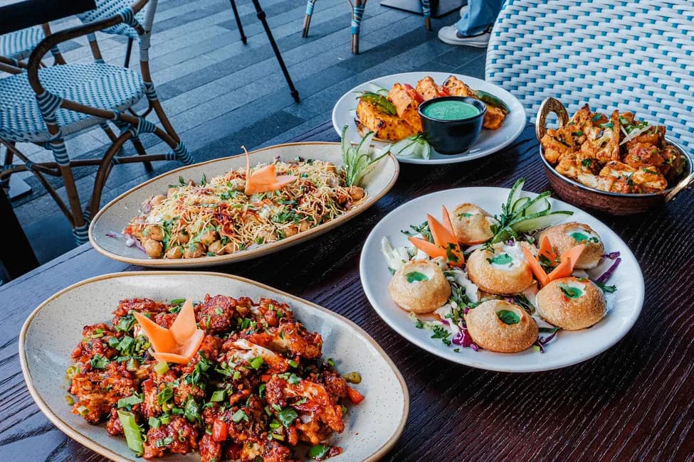 North Indian restaurant dishes displayed on white plates at an outdoor table with blue chairs