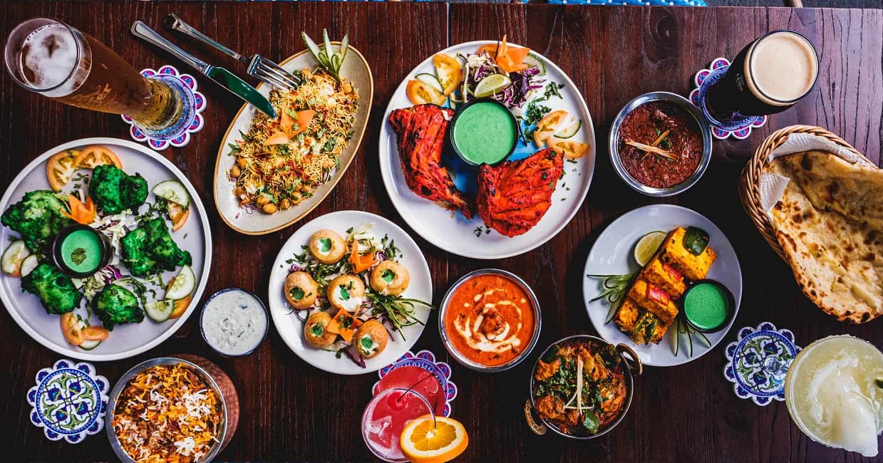 Overhead view of North Indian dishes including tandoori chicken, curries, naan bread, and vegetable preparations with green chutneys