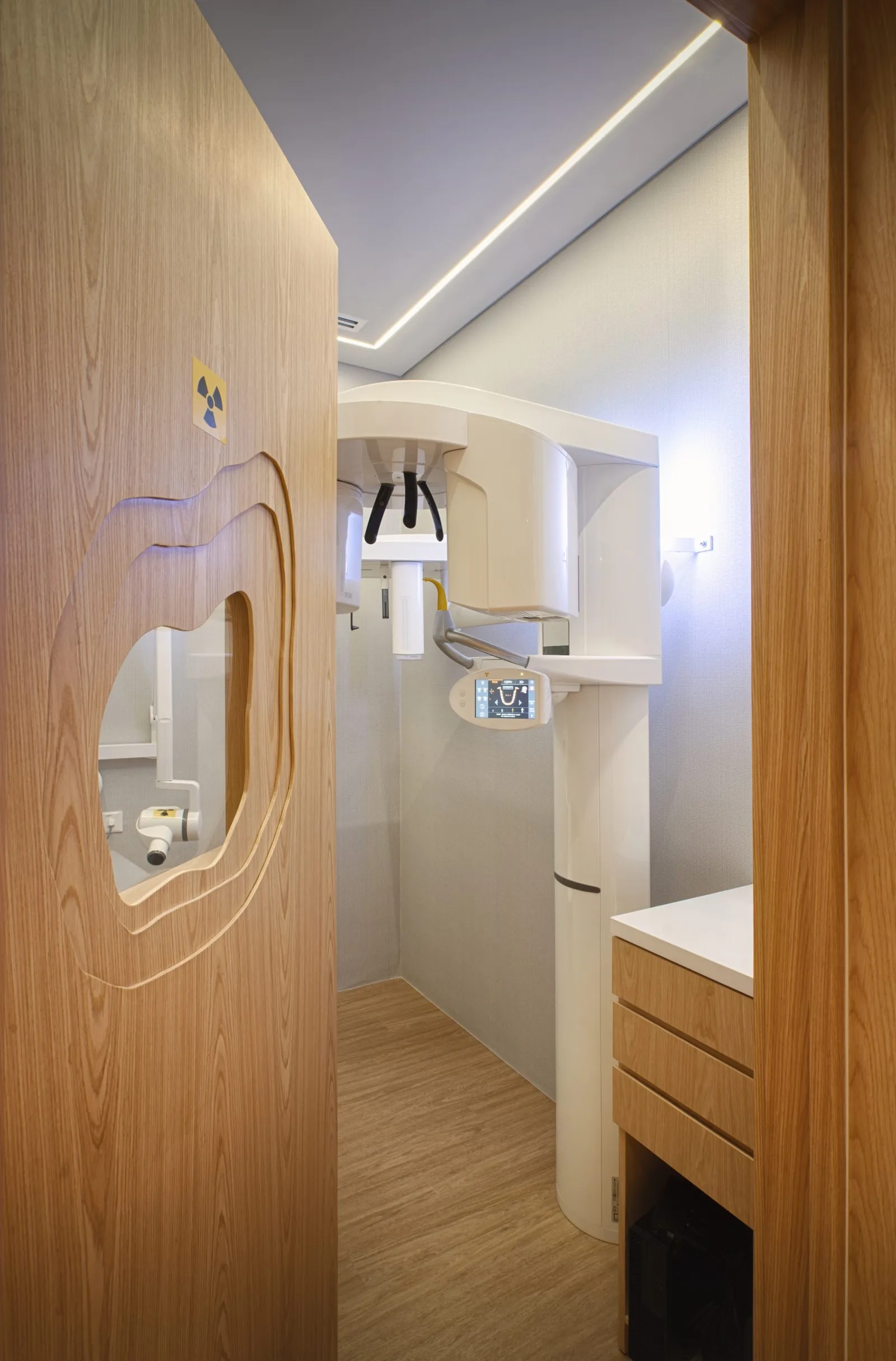 Modern dental treatment room with wood paneling, ceiling lights, and mounted dental equipment