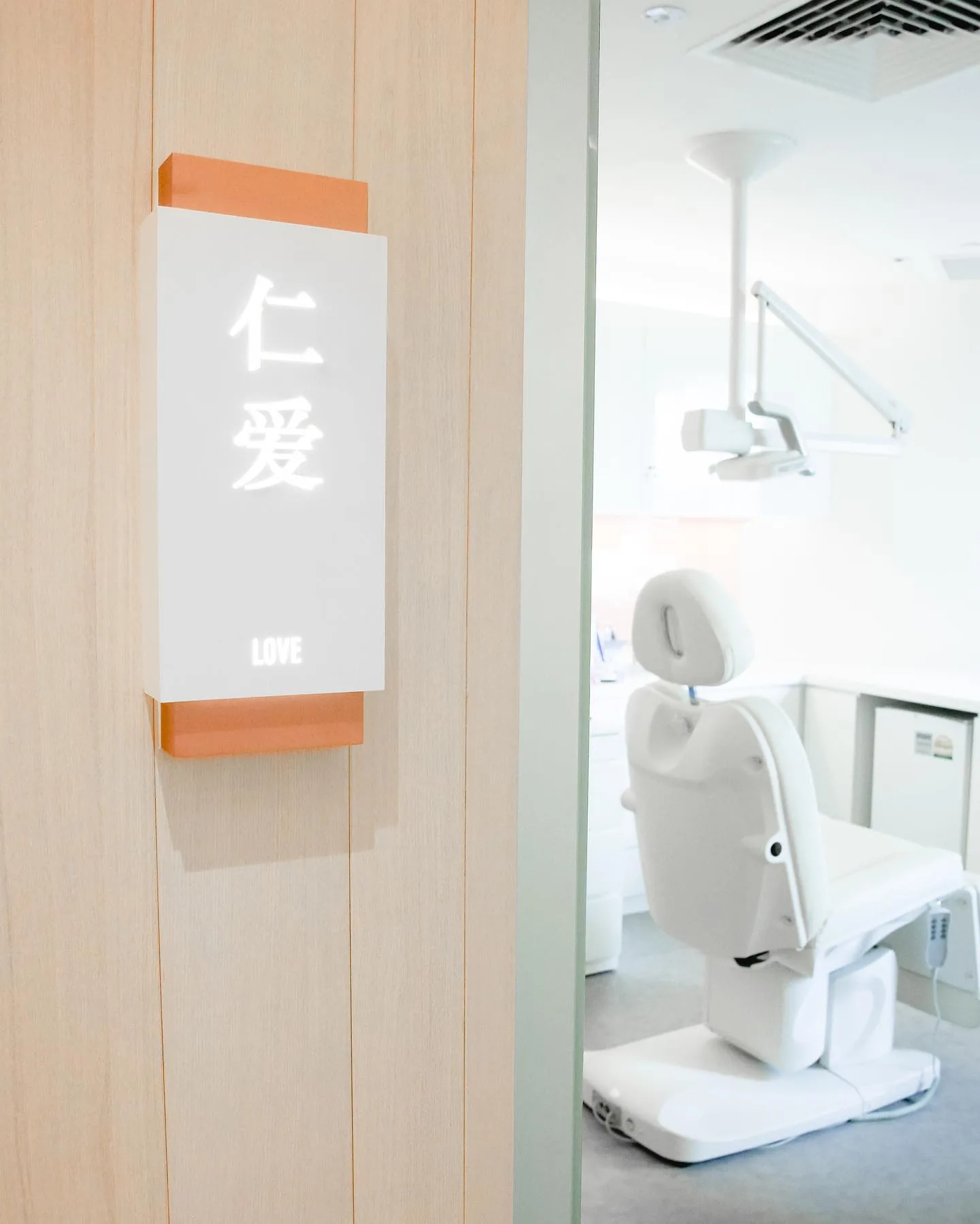 Modern dental clinic treatment room with white chair and equipment visible through glass entrance door