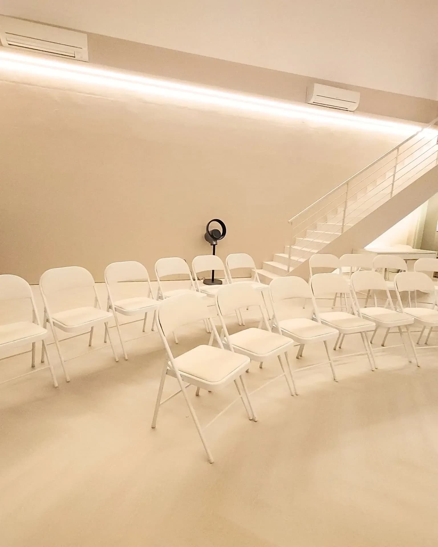White chairs arranged in a spacious, minimalist event room with linear ceiling lights