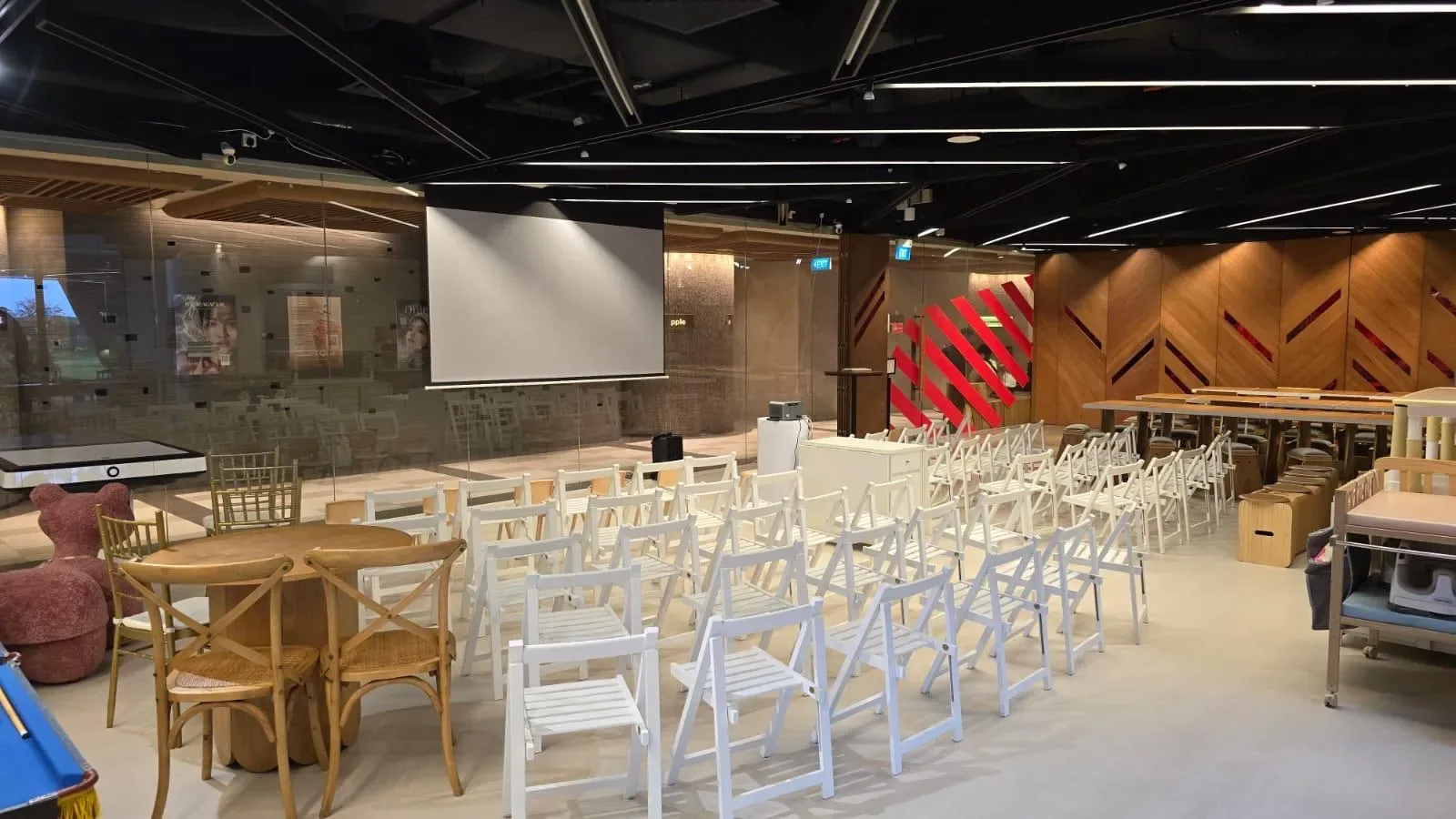 Event venue interior with rows of white and wooden chairs facing a projection screen and decorated walls