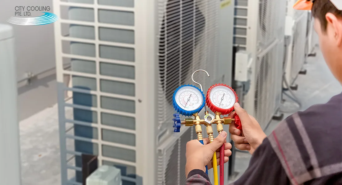 Technician holding red and blue pressure gauges while servicing rooftop air conditioning units