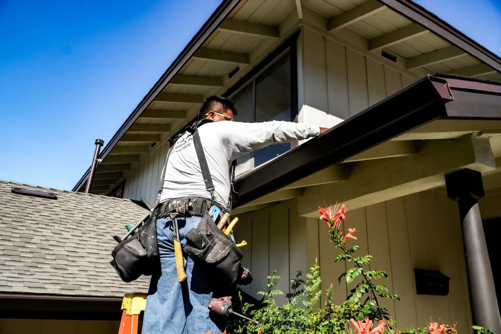 Worker on ladder cleaning gutters along residential home roofline