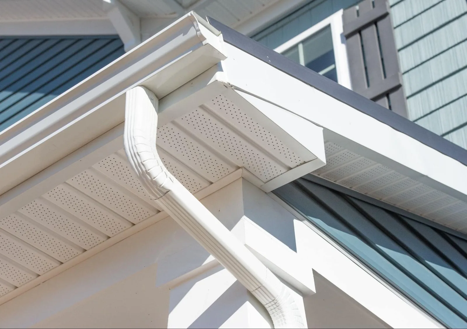 White gutters and downspout installed on house exterior with perforated soffit