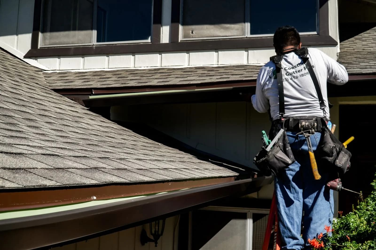 Worker in safety harness cleaning gutters on residential roofline