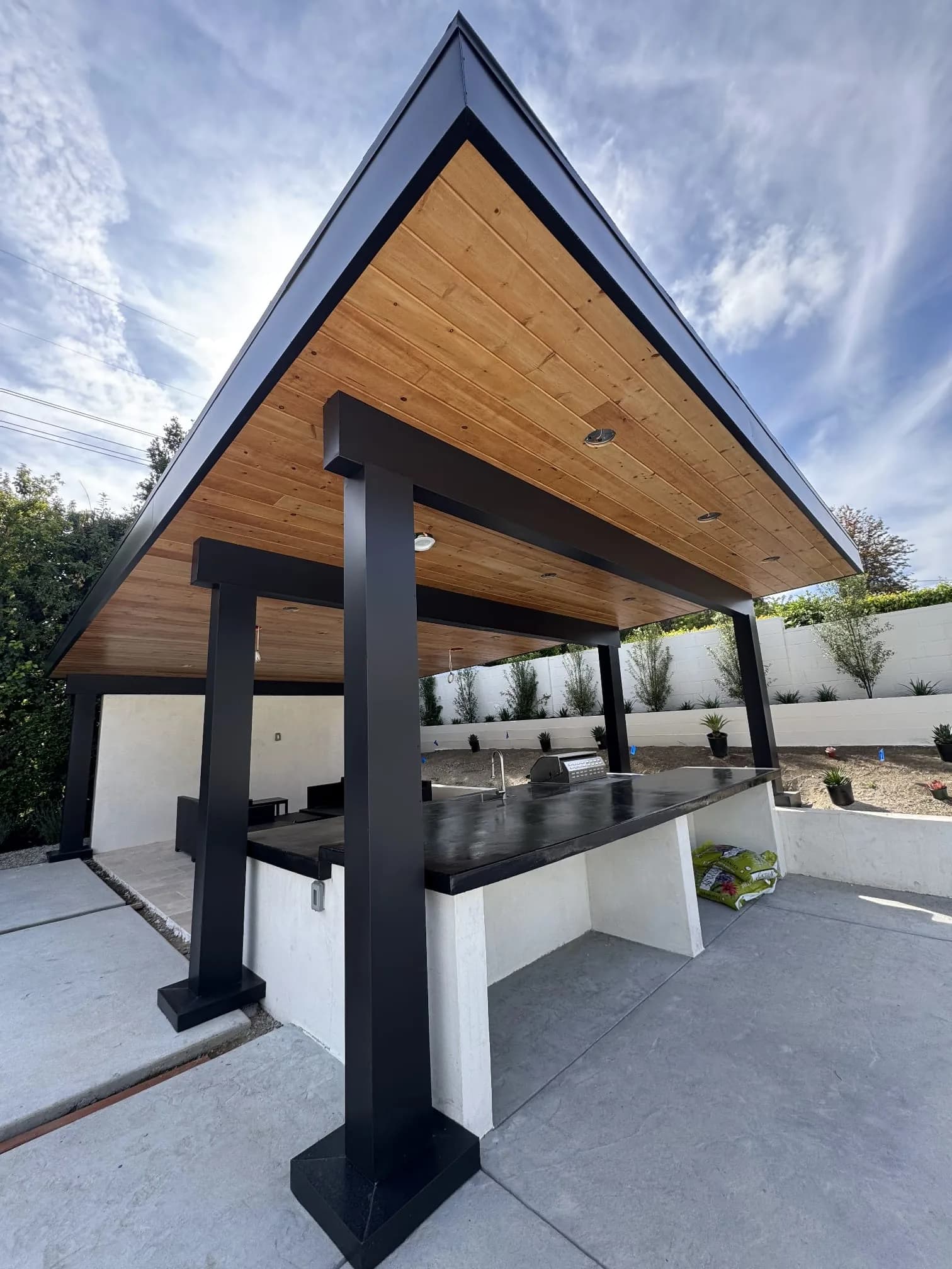 Modern outdoor kitchen pavilion with black steel frame and wood ceiling