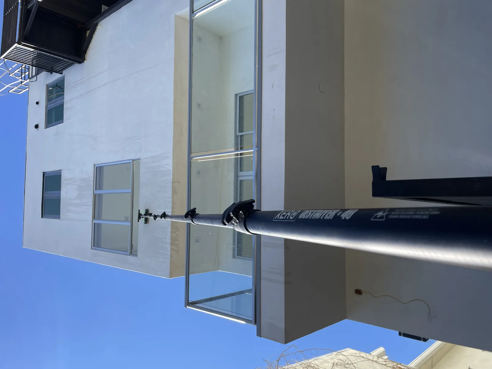 Worker on ladder cleaning gutters on white house exterior