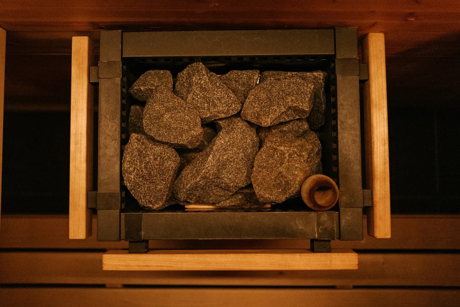 Sauna heater with heated rocks in wooden frame with ladle
