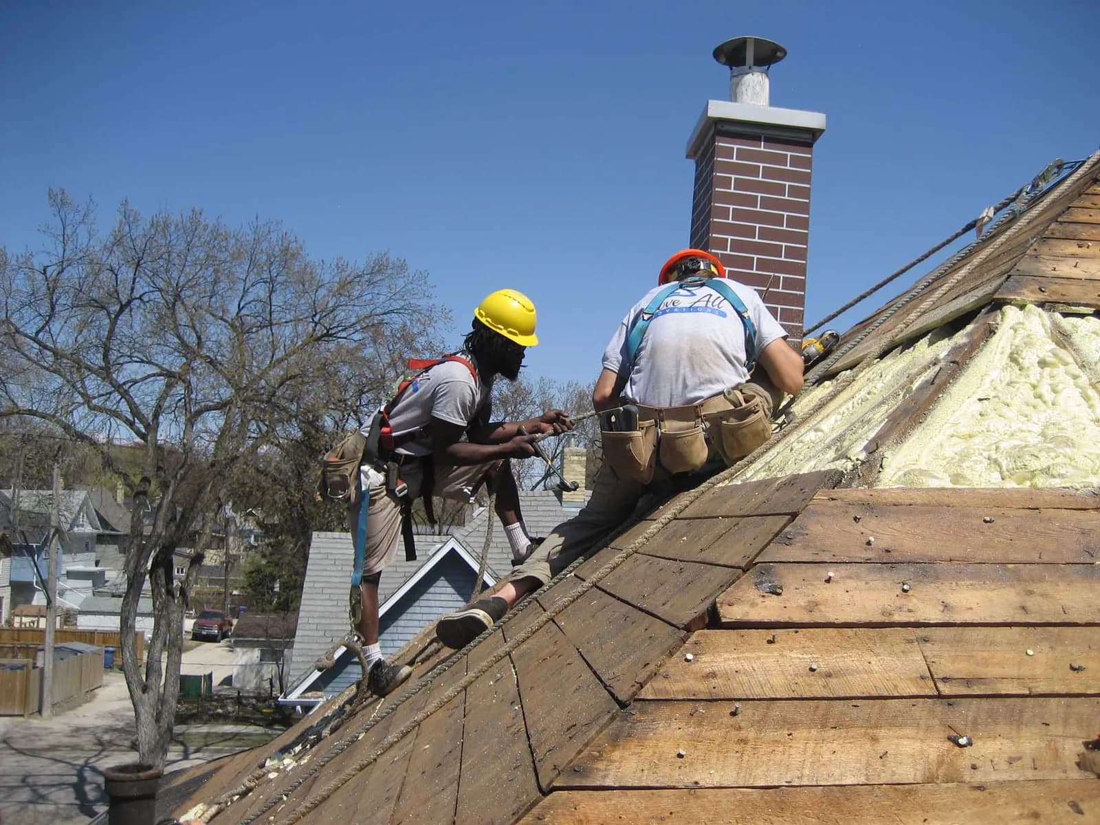 Two roofers in hard hats working on wooden shingle roof replacement.