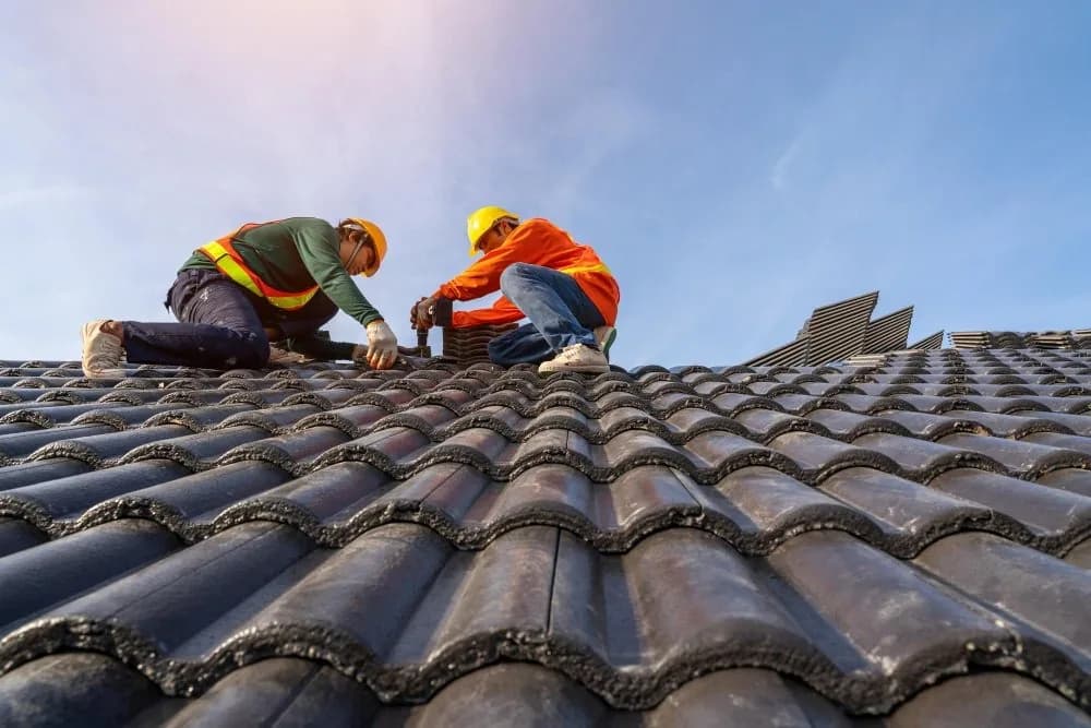 Roofing workers in hard hats and safety vests working on a clay tile roof