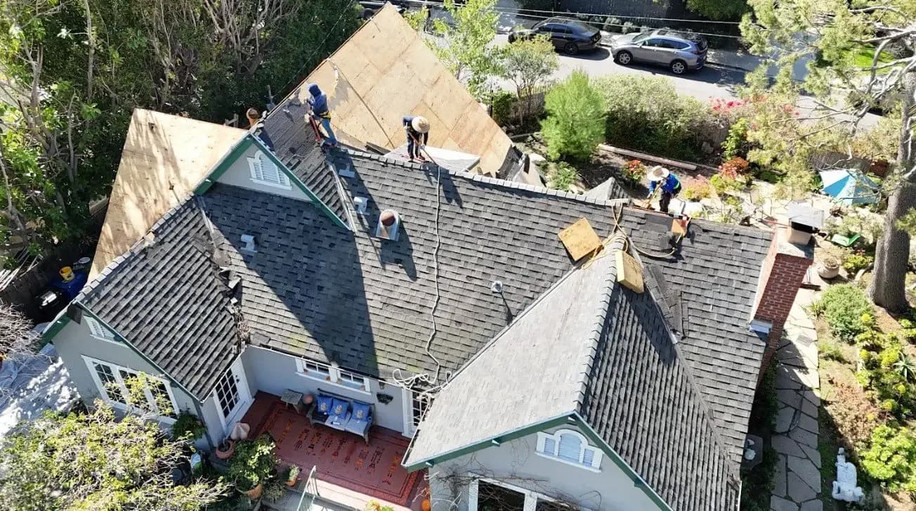 Aerial view of roofing crew working on residential roof replacement with multiple workers on pitched shingles