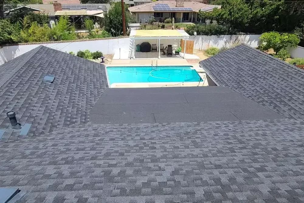Newly installed dark gray asphalt shingle roof on residential home with pool below
