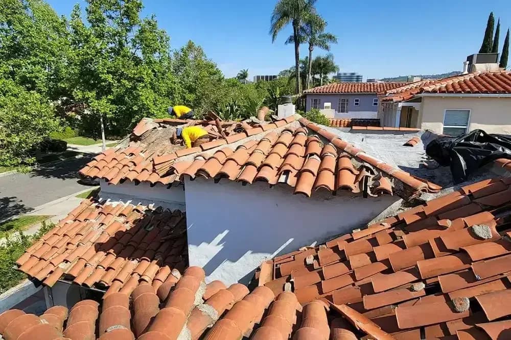 Roofers replacing terracotta clay tiles on a residential roof during active construction