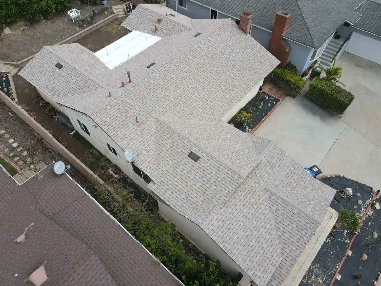 Aerial view of completed residential roof with new gray asphalt shingles and brick chimneys