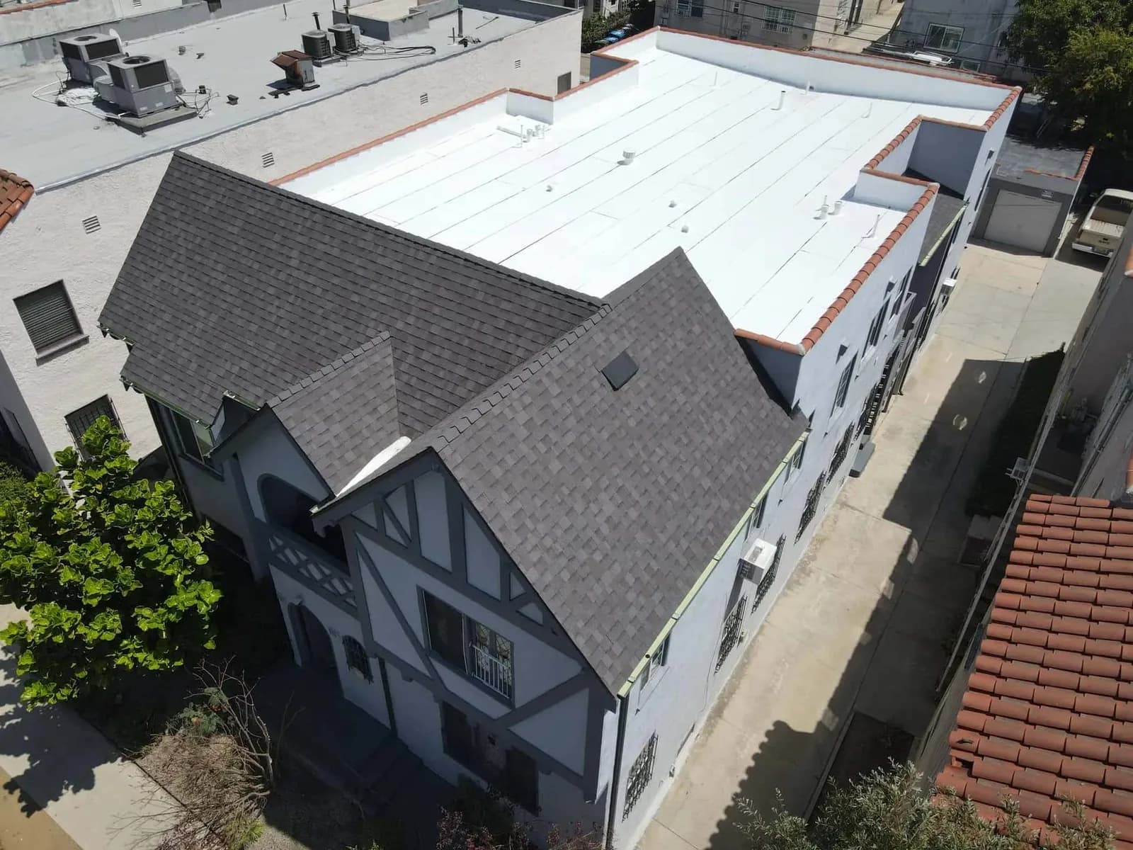 Aerial view of residential building showcasing newly installed dark gray shingle roof and white flat roofing