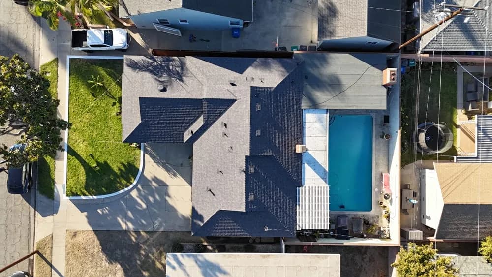 Aerial view of house with dark roof, white trim, and turquoise door among neighboring properties