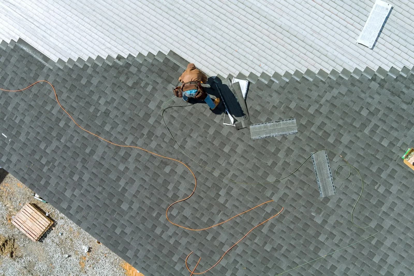 Roofer in safety harness installing shingles on residential roof