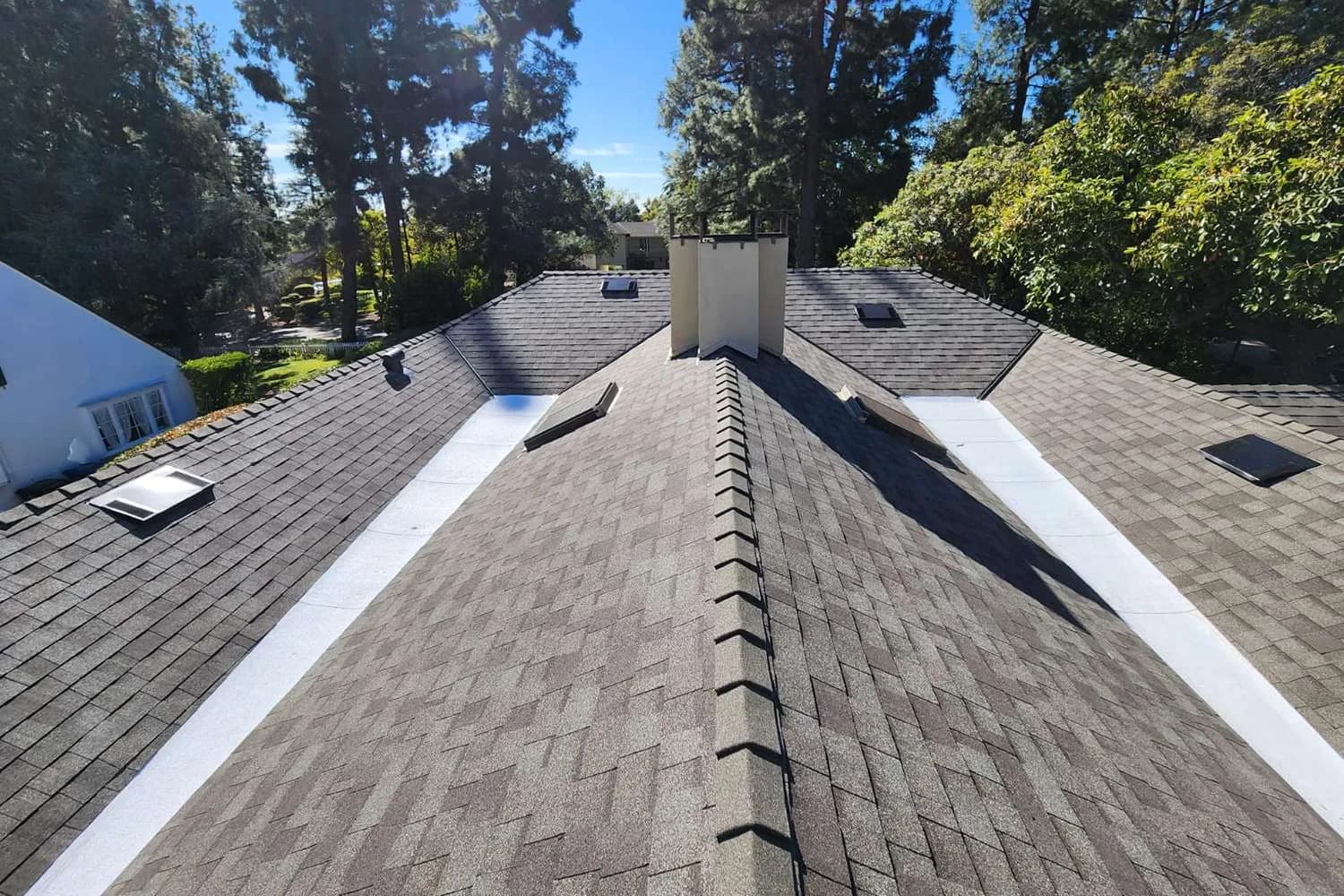 Completed asphalt shingle roof installation with white ridge trim and chimney flashing